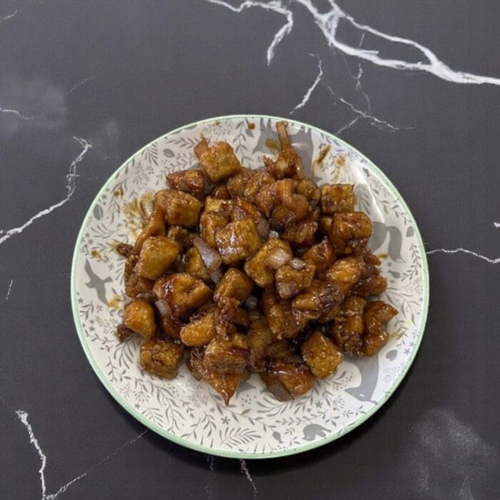 A marble counter features a plate of fried chicken, enhanced with SpicyMama Mammy Sauce for a spicy kick.