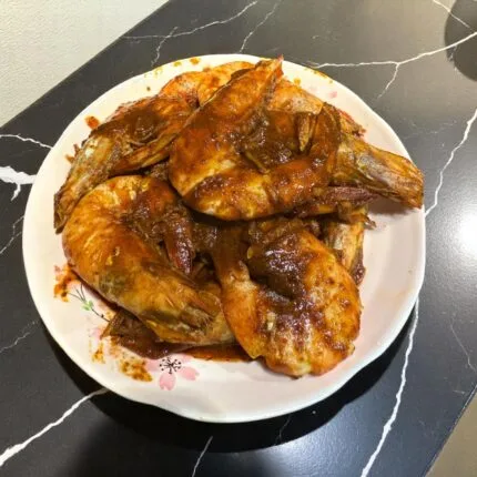 A plate of cooked shrimp with Kam Hiong sauce displayed on a kitchen counter.