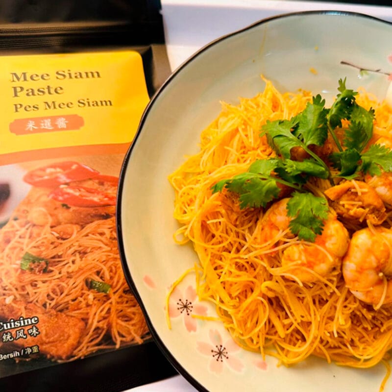 A plate of Spicymama Mee Siam featuring noodles topped with shrimp and fresh herbs, beautifully presented.