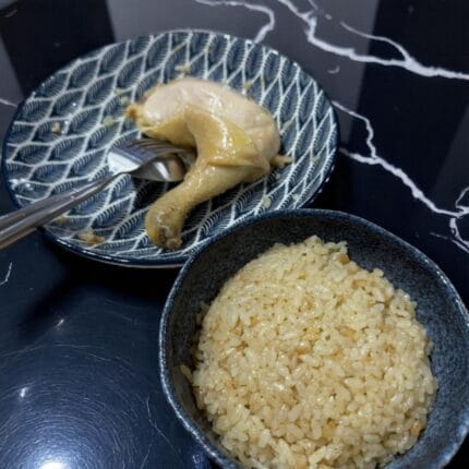 A bowl of rice with a piece of chicken on a table, labeled as SpicyMama Chicken Rice.