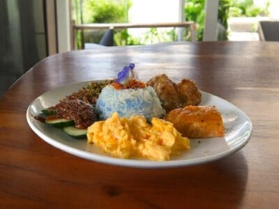 A beautifully arranged plate of Spicymama Anchovy Nasi Lemak on a wooden table, highlighting its rich ingredients and presentation.