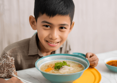 A smiling boy holds a bowl of soup, showcasing joy and warmth in a cozy setting. Ramadan Iftar