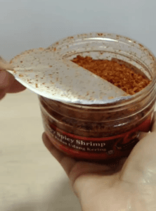 A person holding a jar of Spicymama, showcasing the vibrant red spice against a neutral background.