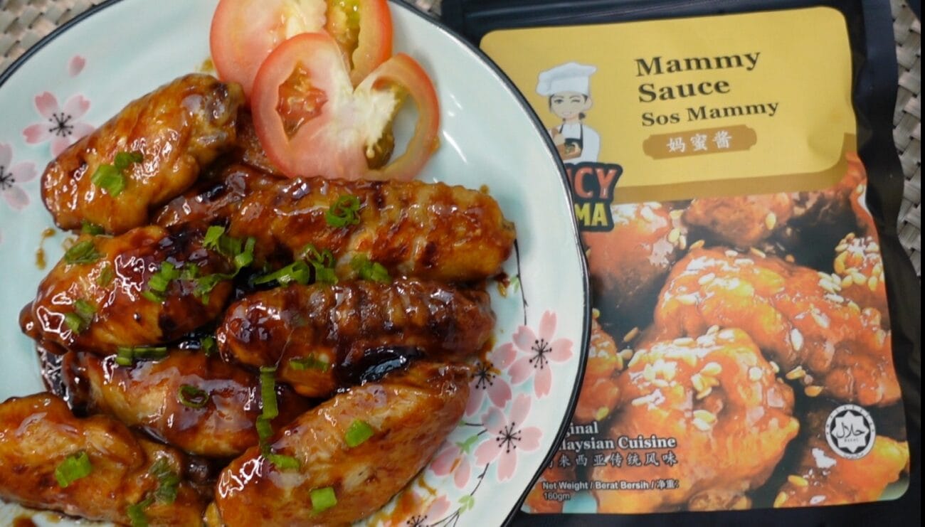 A plate of chicken wings coated in sauce, accompanied by a packet of Mammy Sauce for dipping.