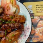 A plate of chicken wings coated in sauce, accompanied by a packet of Mammy Sauce for dipping.