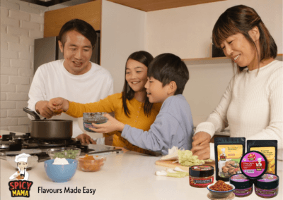 A family gathers in the kitchen, preparing food together using SpicyMama condiments for added asian flavors.