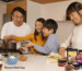A family gathers in the kitchen, preparing food together using SpicyMama condiments for added asian flavors.