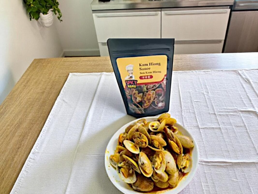 Delicious stir-fried clams in a spicy Kam Hiong sauce, presented with colorful garnishes on a white plate.