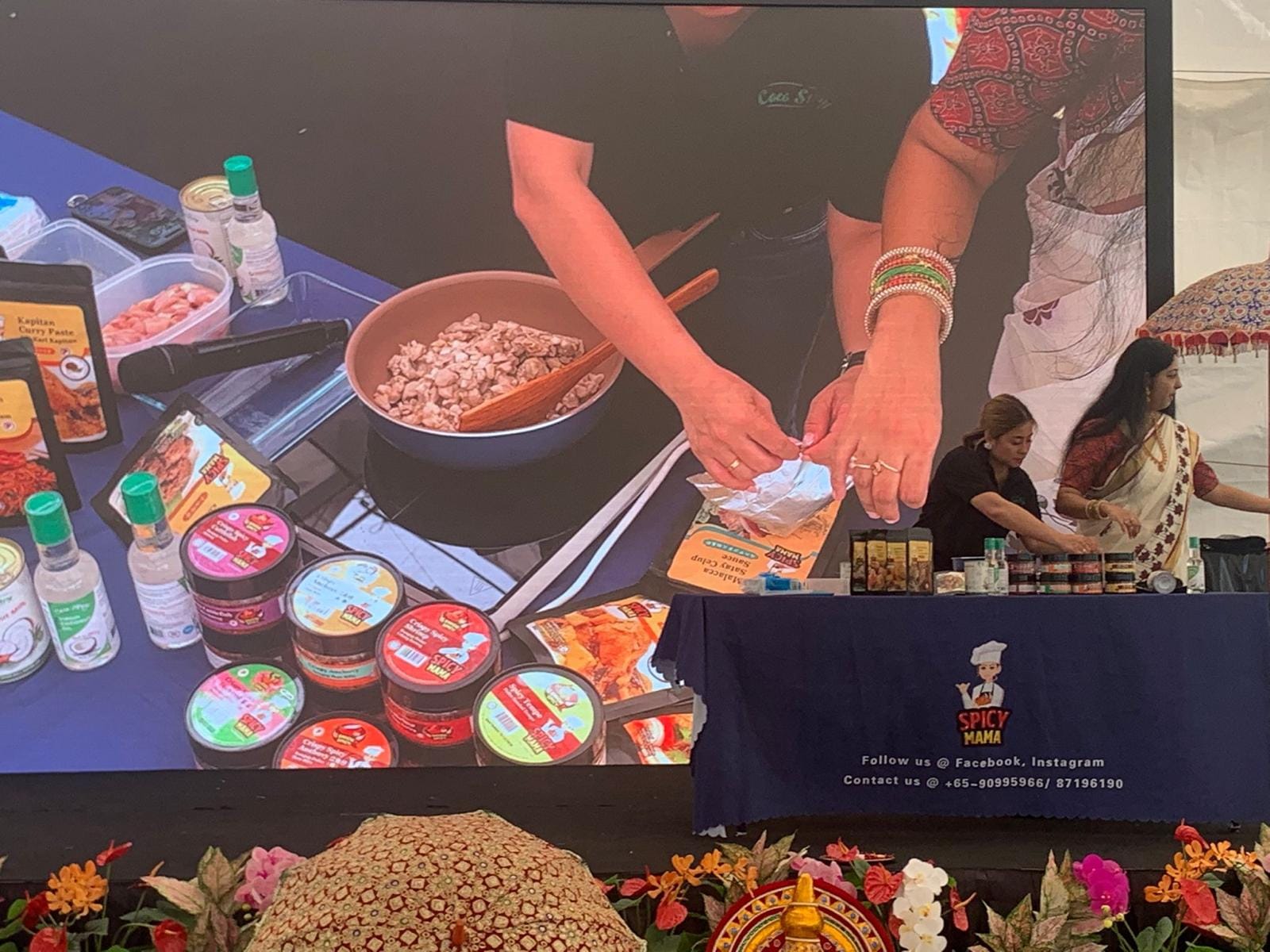 SpicyMama Joins the Festivities at Sakhi Onam 2025 with a Live Food Demo 1 A woman demonstrates food preparation on a large screen at the SpicyMama event for Sakhi Onam celebrations by the Malayalee Association.