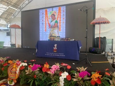 A stage adorned with flowers featuring a woman standing confidently at the center, engaging with the audience.