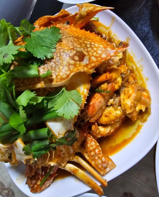 A plate of crab garnished with fresh green herbs, showcasing a vibrant and appetizing seafood dish.Spicymama Kam Hiong Sauce