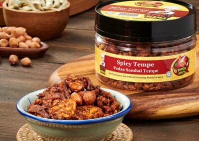 A Wholesome Twist on Local Flavour Tempe 2 A jar filled with spicy tempe is placed on a wooden table, highlighting its rich color and inviting appearance.