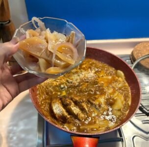 A person holds a bowl of food above a stove, featuring SpicyMama KAM HIONG SAUCE ready for cooking.
